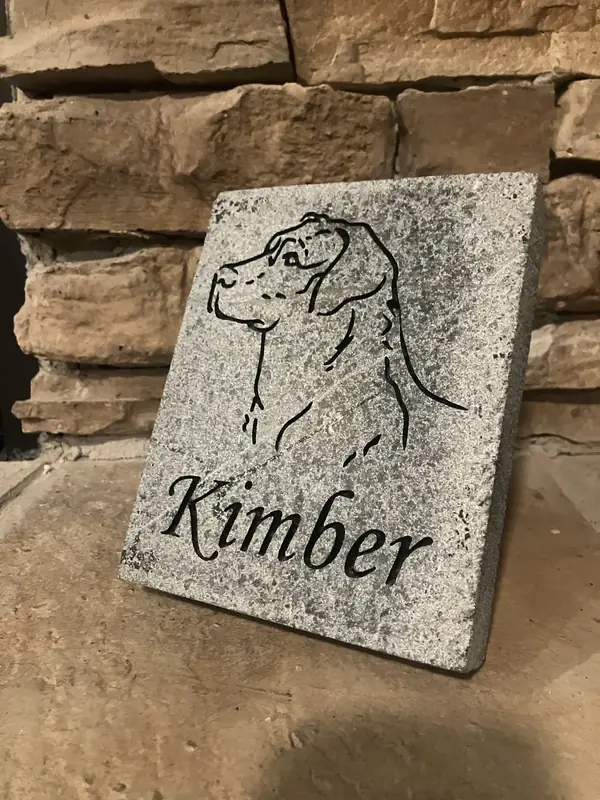 A custom engraved pet memorial stone placed in a garden, honoring a beloved family pet